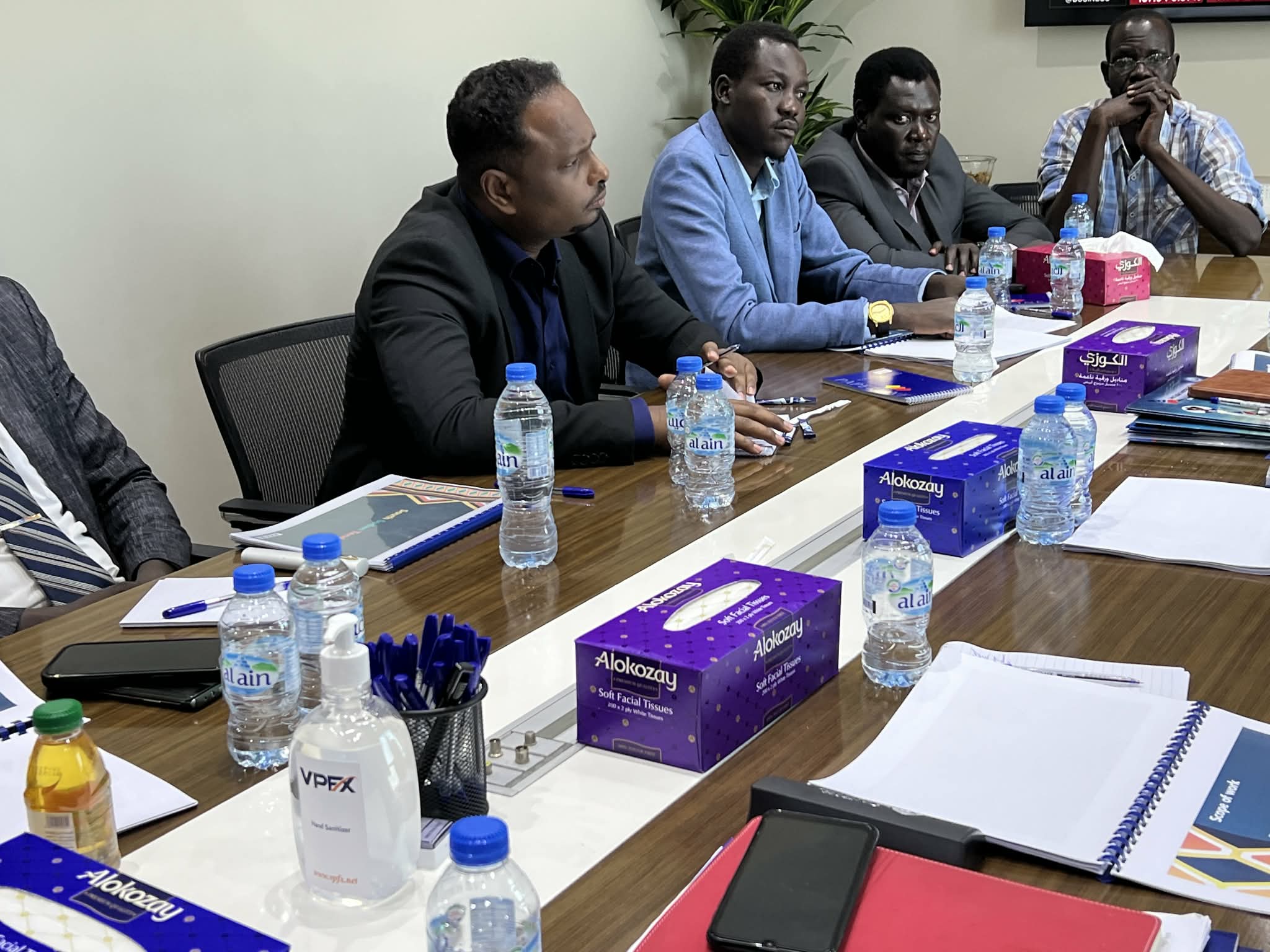 Participants seated at a meeting table with notebooks and documents.