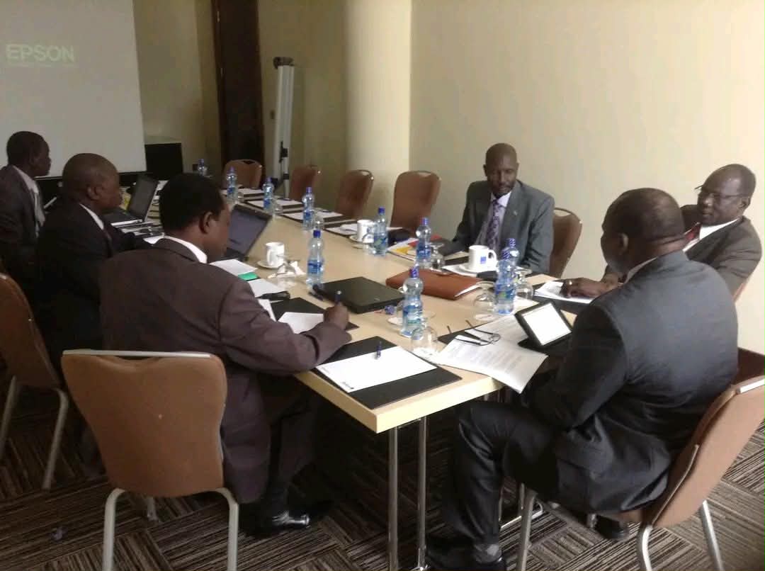 Participants seated around a meeting table with documents and equipment.